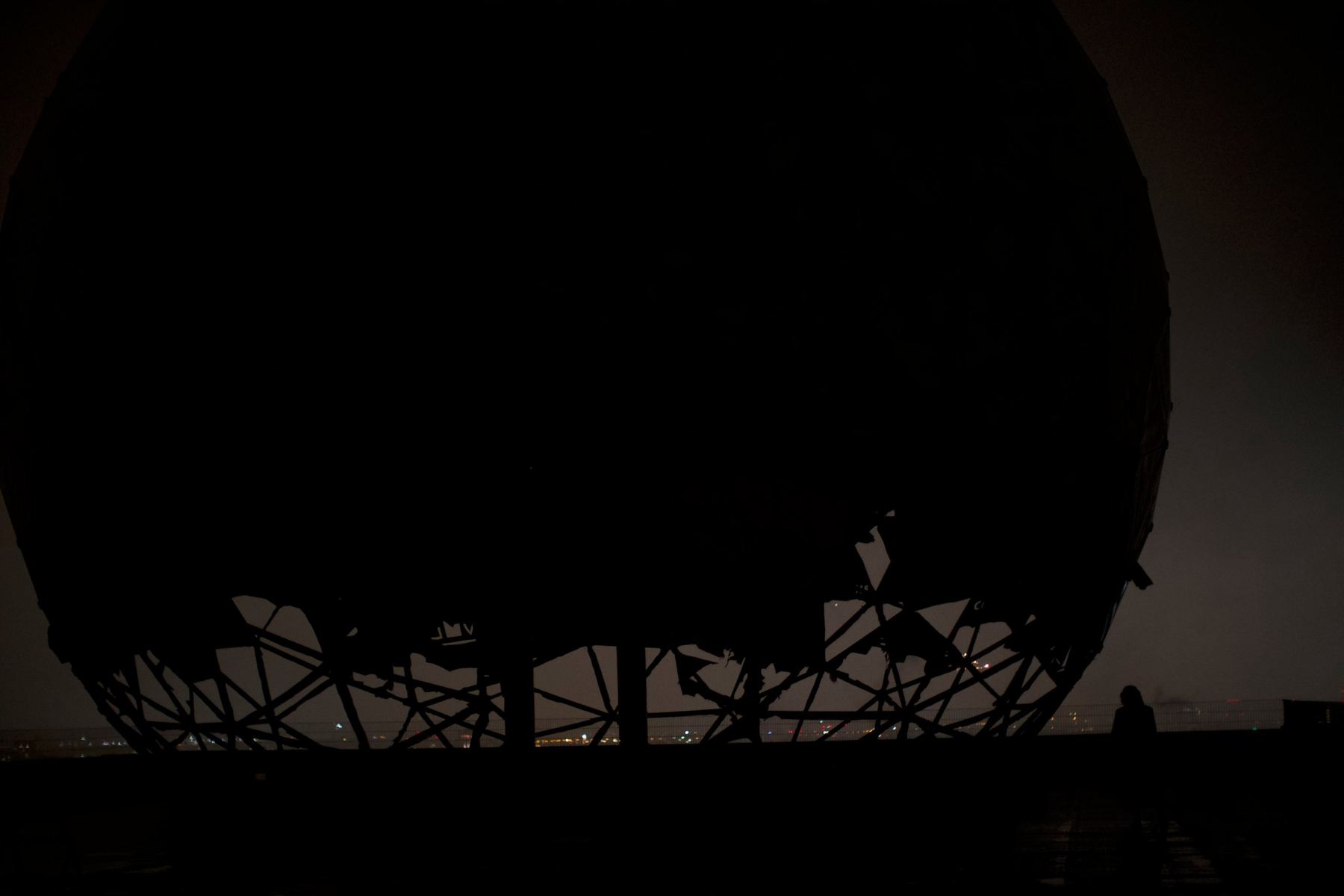 A huge dark dome on a rooftop at night, its broken ribs outlined against the city lights.