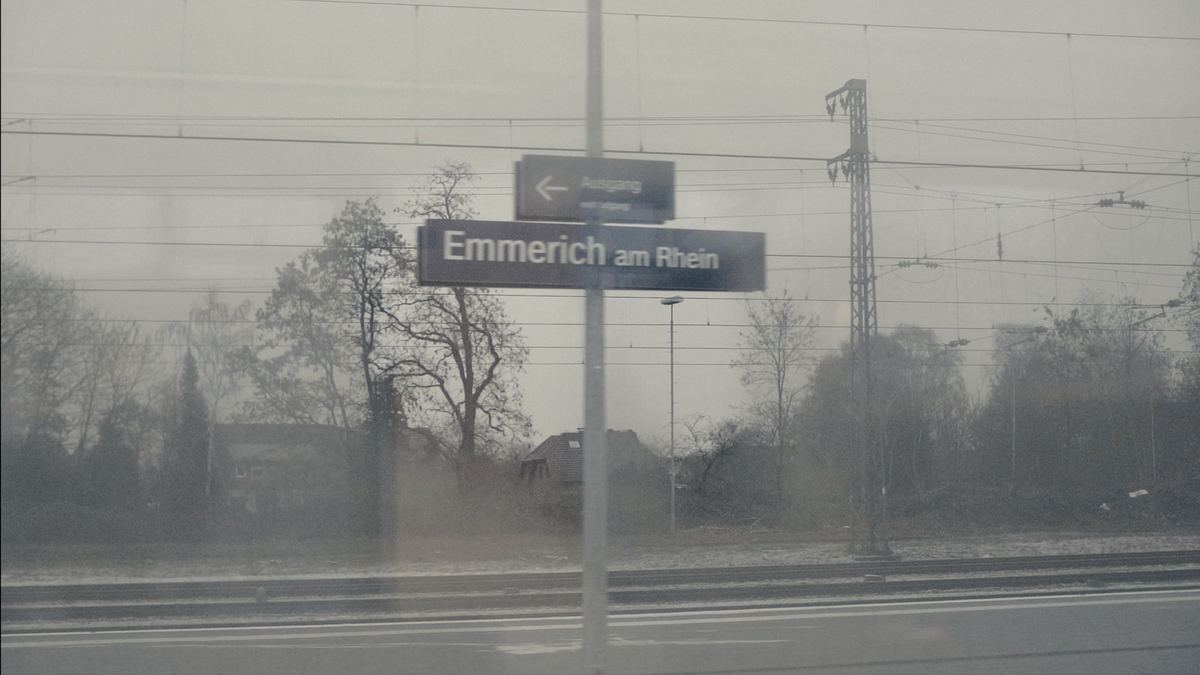 A station sign reading Emmerich am Rhein, seen blurred through a train window.