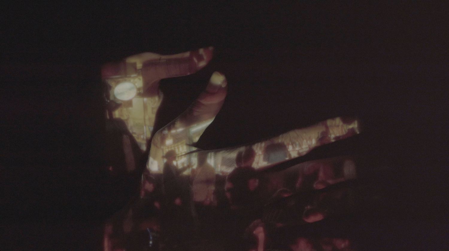 A hand in the dark, a crowded bar scene projected on its fingers.